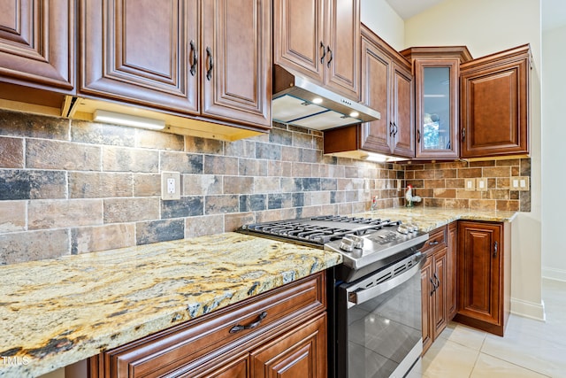 kitchen with light stone counters, tasteful backsplash, light tile patterned floors, stainless steel gas range, and exhaust hood