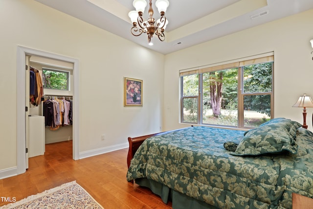 bedroom featuring a tray ceiling, a closet, an inviting chandelier, a walk in closet, and hardwood / wood-style floors