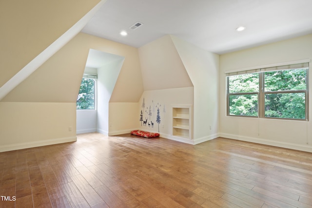 additional living space featuring light wood-type flooring, vaulted ceiling, and built in features