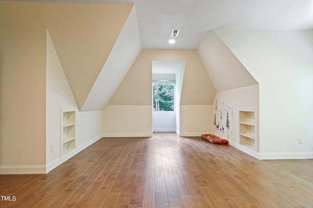 bonus room featuring wood-type flooring, built in shelves, and lofted ceiling