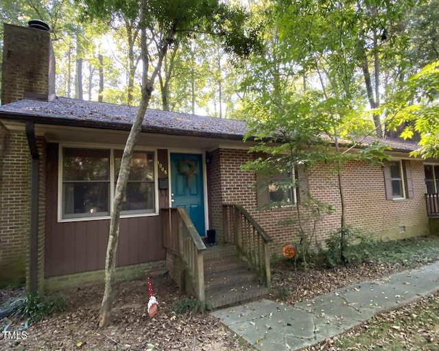 view of front of property featuring brick siding, crawl space, and a chimney