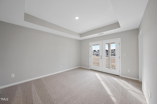 empty room featuring a raised ceiling, carpet flooring, and french doors