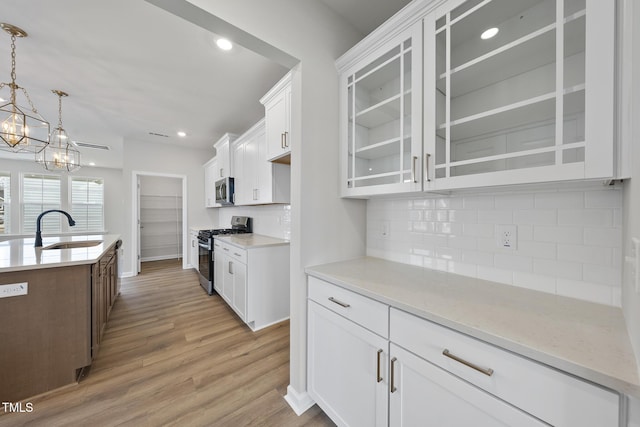 kitchen with appliances with stainless steel finishes, sink, white cabinets, hanging light fixtures, and light hardwood / wood-style flooring