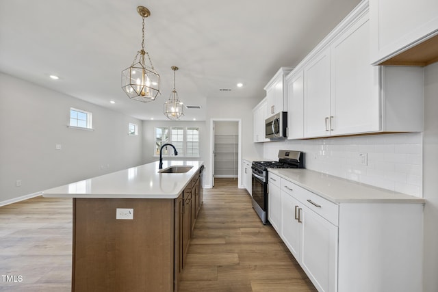 kitchen with appliances with stainless steel finishes, sink, white cabinets, hanging light fixtures, and a kitchen island with sink