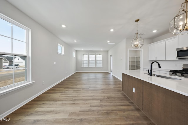 kitchen with sink, white cabinets, hanging light fixtures, range, and light wood-type flooring