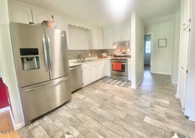 kitchen with appliances with stainless steel finishes, decorative backsplash, white cabinetry, and light hardwood / wood-style flooring