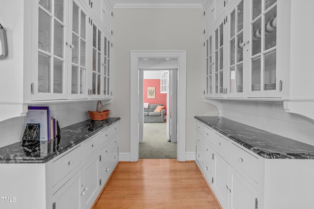 kitchen featuring decorative backsplash, light hardwood / wood-style flooring, dark stone countertops, crown molding, and white cabinets