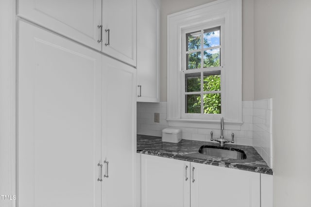 kitchen featuring sink, white cabinetry, backsplash, and dark stone counters