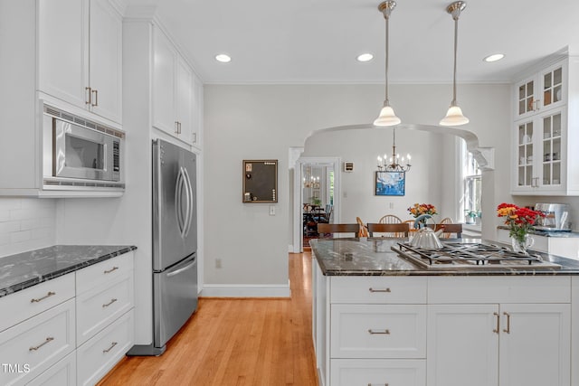 kitchen with appliances with stainless steel finishes, decorative light fixtures, dark stone counters, white cabinets, and light hardwood / wood-style flooring