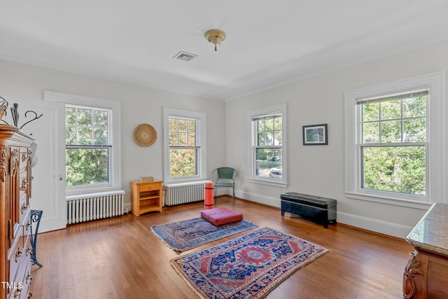 living area with ornamental molding, radiator heating unit, and hardwood / wood-style floors