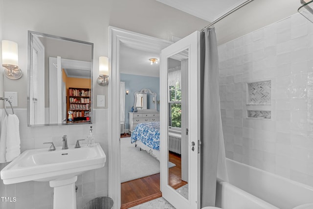 bathroom featuring hardwood / wood-style flooring, shower / bathtub combination with curtain, ornamental molding, and tile walls