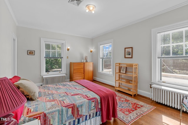 bedroom with multiple windows, radiator heating unit, and hardwood / wood-style flooring