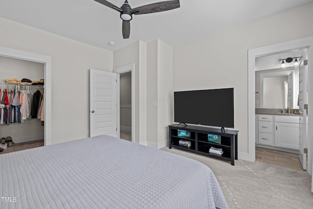 bedroom featuring ceiling fan, light carpet, a spacious closet, a closet, and ensuite bath