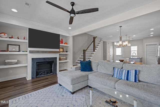 living room with wood-type flooring, ceiling fan with notable chandelier, built in features, and sink