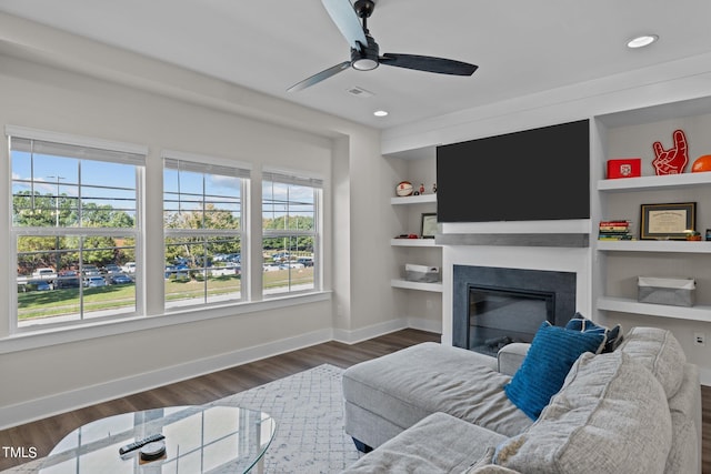 living room featuring dark wood-type flooring, built in shelves, and ceiling fan