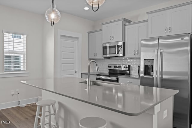 kitchen featuring appliances with stainless steel finishes, a kitchen bar, decorative light fixtures, and a center island with sink