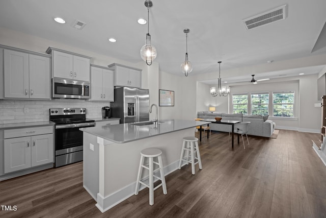 kitchen featuring decorative light fixtures, a kitchen island with sink, stainless steel appliances, dark hardwood / wood-style floors, and a breakfast bar