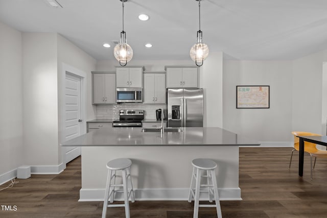 kitchen featuring a kitchen island with sink, pendant lighting, sink, stainless steel appliances, and a kitchen bar