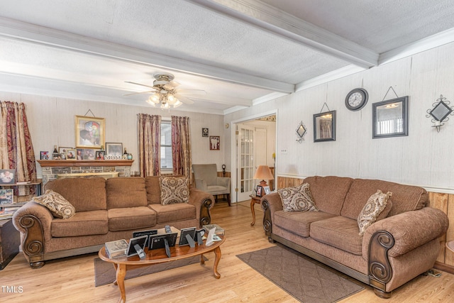 living area featuring beamed ceiling, ceiling fan, light wood-style flooring, and ornamental molding