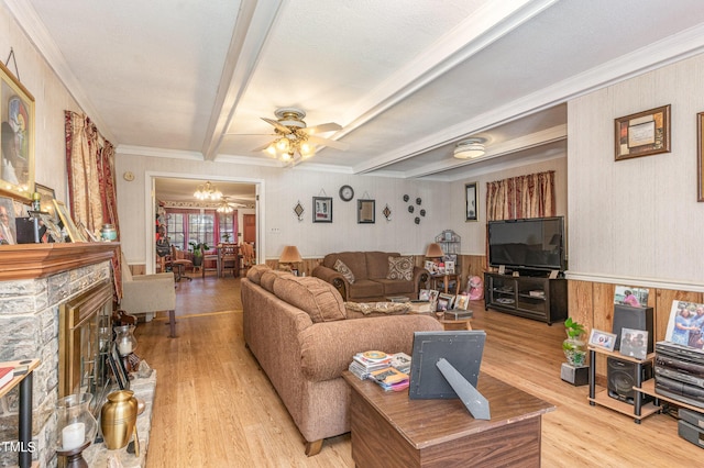 living room with light wood finished floors, a stone fireplace, ornamental molding, beamed ceiling, and ceiling fan with notable chandelier