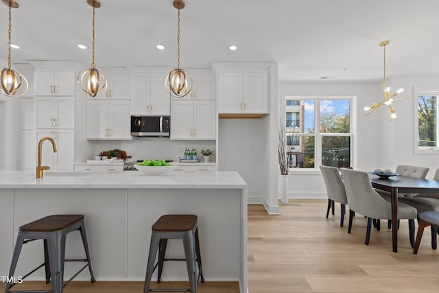 kitchen featuring decorative light fixtures, a kitchen island with sink, backsplash, white cabinetry, and sink