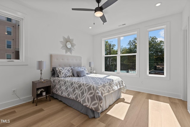 bedroom featuring ceiling fan, light hardwood / wood-style floors, and multiple windows