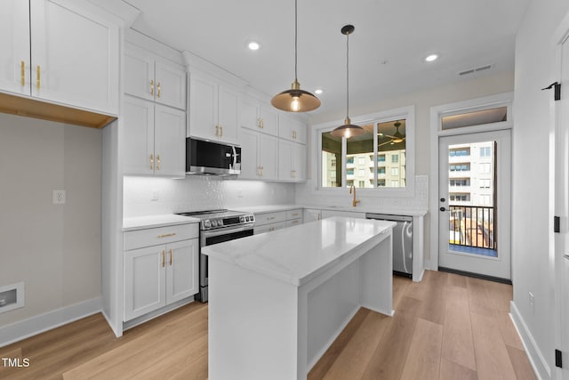 kitchen featuring white cabinets, stainless steel appliances, hanging light fixtures, and a center island