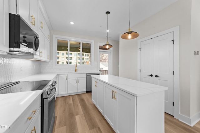 kitchen with hanging light fixtures, stainless steel appliances, white cabinets, a center island, and sink