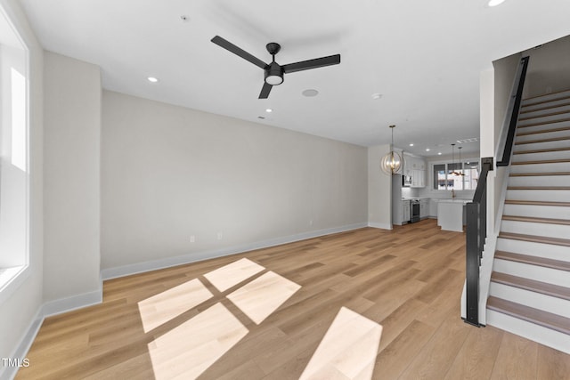 unfurnished living room with ceiling fan with notable chandelier and light wood-type flooring