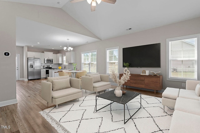 living room featuring lofted ceiling, light wood-type flooring, and ceiling fan with notable chandelier