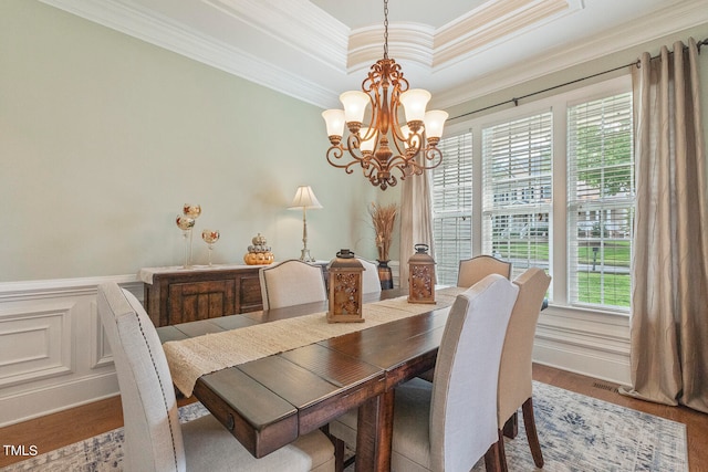 dining room with a tray ceiling, wood-type flooring, ornamental molding, and an inviting chandelier