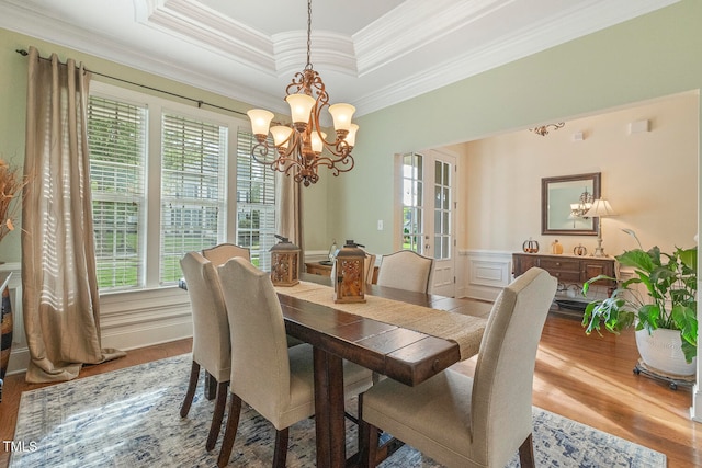 dining space with crown molding, a notable chandelier, a raised ceiling, and hardwood / wood-style floors