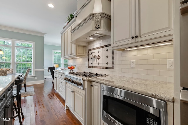 kitchen featuring light stone countertops, stainless steel appliances, custom exhaust hood, crown molding, and dark hardwood / wood-style floors