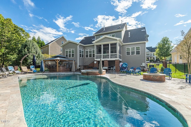 back of property with a patio, a sunroom, a gazebo, an outdoor fire pit, and a swimming pool with hot tub