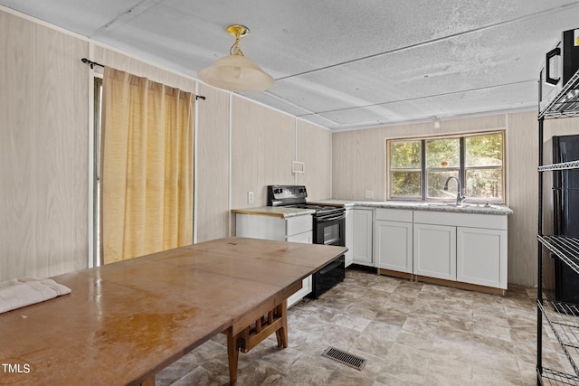 kitchen featuring pendant lighting, wooden walls, white cabinetry, and black / electric stove