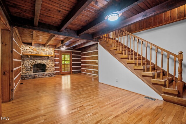 unfurnished living room with beam ceiling, a stone fireplace, light hardwood / wood-style flooring, and wood ceiling