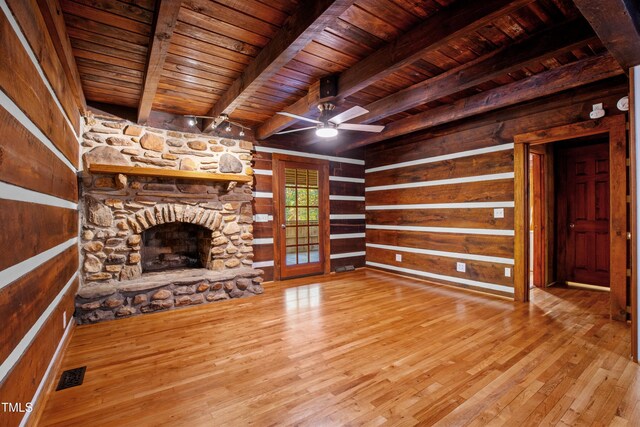 unfurnished living room featuring a stone fireplace, wood ceiling, hardwood / wood-style flooring, beamed ceiling, and ceiling fan