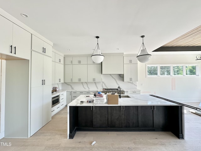 280 Forest Bridge Rd, Youngsville, NC 27596 - kitchen featuring white cabinetry, a kitchen island with sink, light wood finished floors, hanging light fixtures, and light stone counters