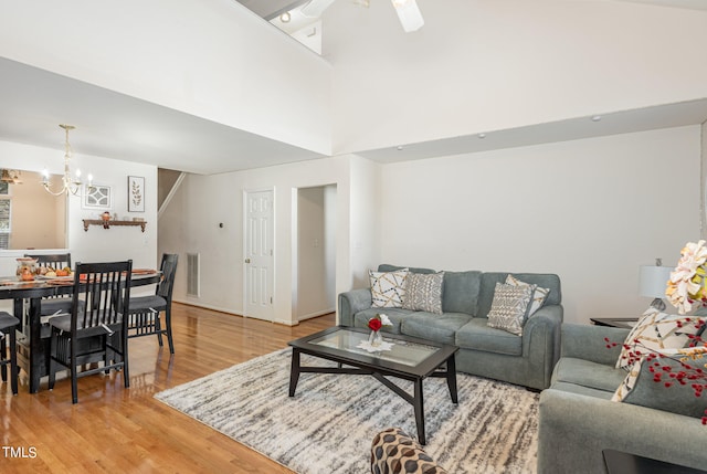 living room with ceiling fan with notable chandelier, a high ceiling, and hardwood / wood-style flooring