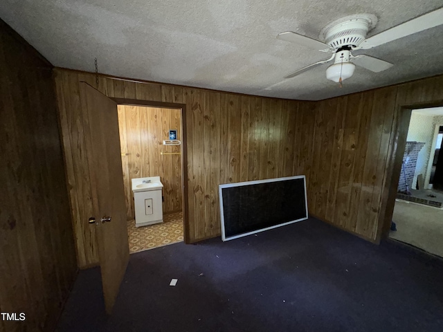 unfurnished bedroom featuring ceiling fan, ensuite bath, wood walls, and a textured ceiling