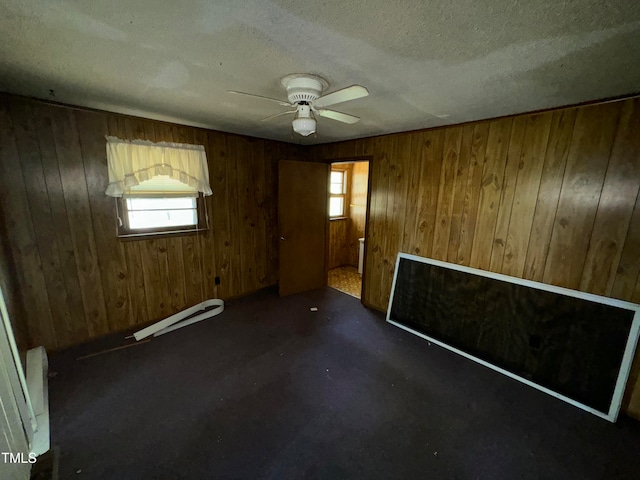 carpeted spare room with a baseboard radiator, plenty of natural light, and wood walls