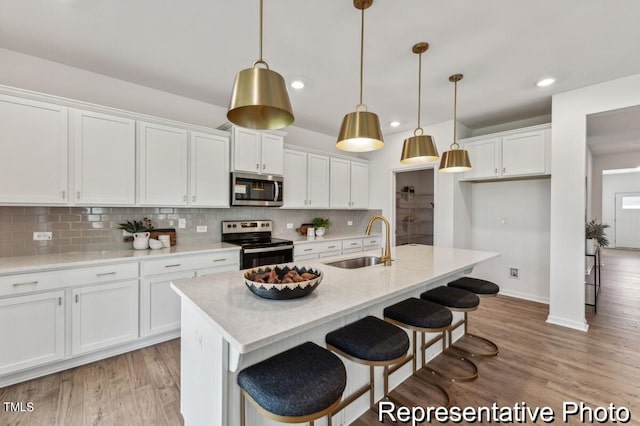 kitchen with pendant lighting, sink, white cabinetry, stainless steel appliances, and a center island with sink