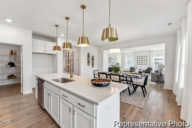 kitchen with pendant lighting, light hardwood / wood-style floors, a kitchen island with sink, sink, and white cabinetry