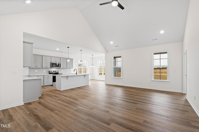 unfurnished living room featuring hardwood / wood-style flooring, high vaulted ceiling, ceiling fan, and sink