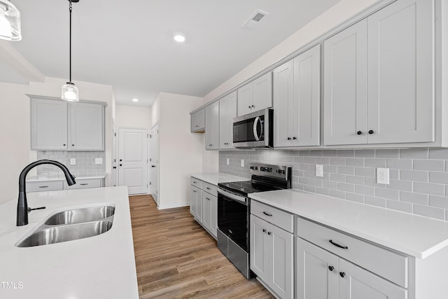 kitchen featuring light wood-type flooring, backsplash, stainless steel appliances, sink, and decorative light fixtures