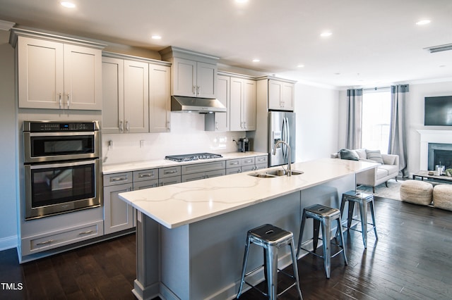 kitchen with sink, gray cabinetry, dark wood-type flooring, stainless steel appliances, and a kitchen breakfast bar