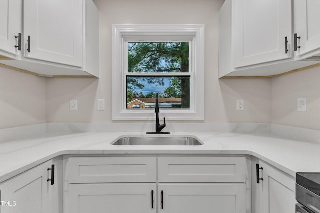 kitchen with light stone counters, white cabinetry, and a sink
