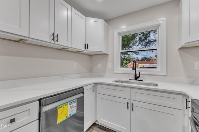 kitchen with light stone countertops, stainless steel dishwasher, a sink, and white cabinetry