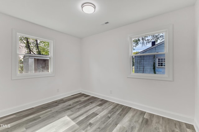 empty room featuring baseboards, a healthy amount of sunlight, wood finished floors, and visible vents