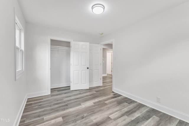 unfurnished bedroom featuring wood finished floors, a closet, and baseboards